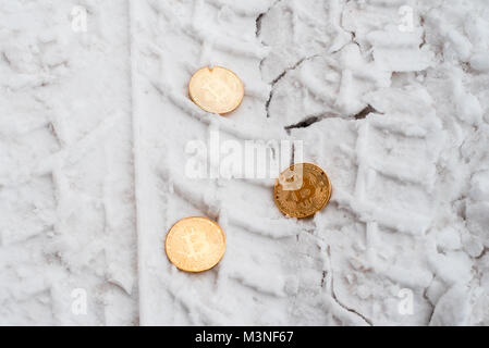 Copprito monete d'oro bitcoin sono distesi sulla neve. Nessuno bisogno. In inverno sulla strada, tracce di vetture. Foto Stock