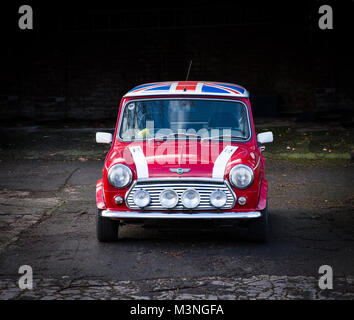 Una vista frontale di un classico, Red Mini Cooper con una bandiera dell'Union Jack sul tetto e di un grande chrome fari anteriori su uno sfondo scuro. Foto Stock