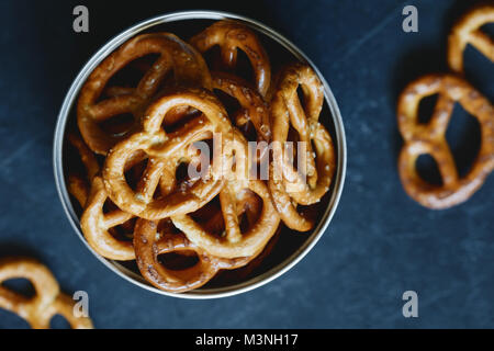 Pretzel croccanti stuzzichini in un vaso di metallo su sfondo nero. Vista dall'alto. Foto Stock