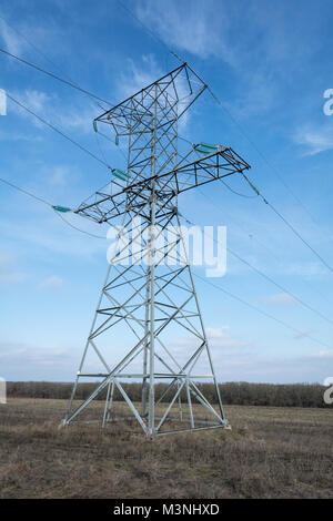 Le linee di alta tensione e tralicci elettrici in un paesaggio agricolo con cirrus nuvole sul cielo blu in inverno Foto Stock