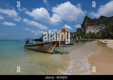 Lo straordinario paesaggio vista di una fila di coda lunga barche ancorato su di una splendida spiaggia di sabbia dorata in Thailandia con il blu del cielo e le torreggianti scogliere Foto Stock