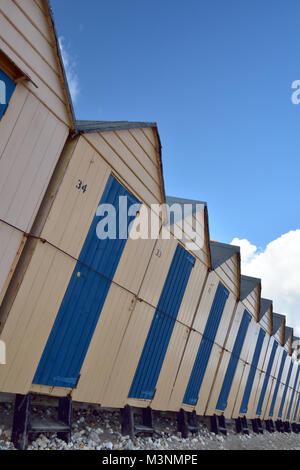 Una riga o linea di blu e bianca spiaggia di capanne contro un cielo blu. chalets per le vacanze e capannoni o capanne in riva al mare su un estati giornata soleggiata. riga dinamico. Foto Stock