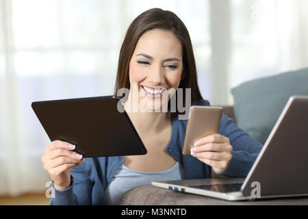 Donna felice utilizzando più dispositivi su un divano nel salotto di casa Foto Stock