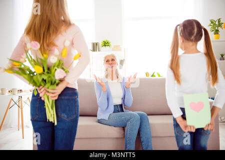 Festa della donna il concetto di comfort. La mamma di tulipani nascondere dietro la schiena kid card con calore per stupito eccitato allegro stupiti scioccato la nonna Foto Stock