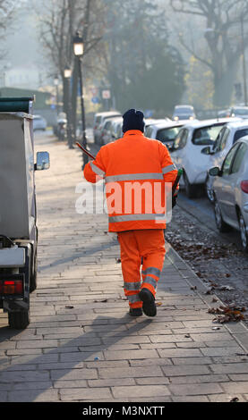Spazzatrice con una camicia arancione che pulisce le strade sporche di una grande città Foto Stock