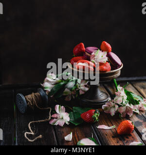 Ciotola con dolci macarons e fragole su un tavolo di legno con fiori Foto Stock