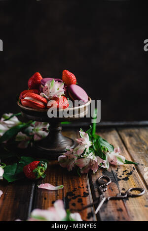 Ciotola con macarons e fragole su un tavolo di legno con fiori e un paio di forbici Foto Stock