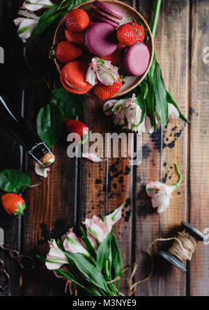 Vista dall'alto di macarons e fragole su un tavolo di legno con fiori, filetti e bottiglia di champagne per il giorno di san valentino Foto Stock