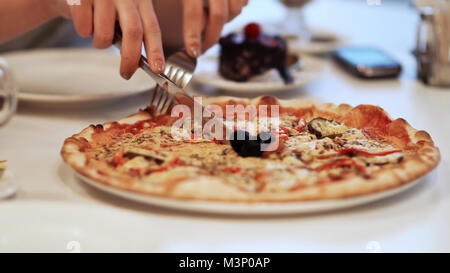 Close-up di un fresco pizze, ragazza taglia la pizza. Foto Stock