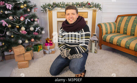 Un giovane ragazzo si siede sul pavimento della sua casa. Tema Natale. Foto Stock