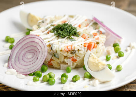Olivier con insalata di trota in una piastra bianca. Tradizionale piatto di russo. Sfondo di legno Foto Stock