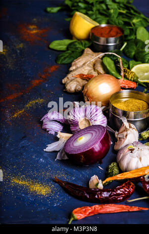 Messa a fuoco selettiva di prezzemolo, basilico, limone, zenzero, peperoni, cipolle e aglio su blu Foto Stock