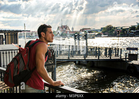 Giovane uomo bello in piedi sul mare guardando intorno alla luce del sole, Bangkok. Foto Stock