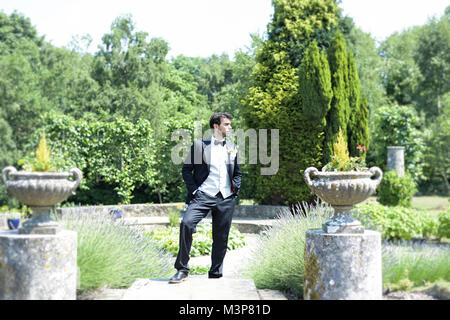 Ritratto di un bello dai capelli scuri giovane in abito nuziale su una luminosa giornata di sole, egli guarda fiducioso e contento Foto Stock