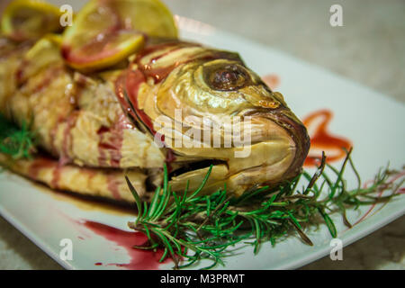 Il pesce con spicchi di limone e un verde rosmarino. Profondità di campo. Foto Stock