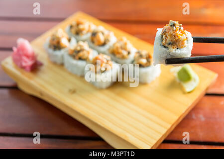 Close up di bastoncini prendendo parte del rotolo di sushi sul tavolo ristorante Foto Stock