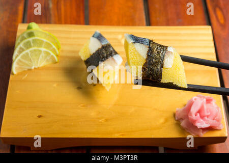 Close up di bastoncini prendendo parte del rotolo di sushi sul tavolo ristorante Foto Stock