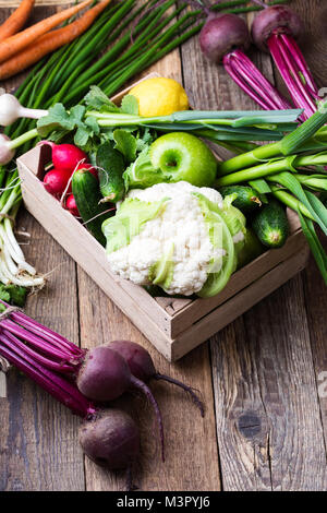 Cassa con diverse farm fresche verdure. Il cavolfiore, aglio, ravanelli, cipolline, beetrots, e cetrioli su rustico sfondo di legno Foto Stock