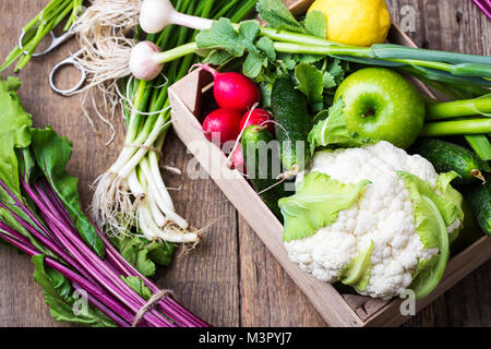 Cassa con diverse farm fresche verdure. Il cavolfiore, aglio, ravanelli, cipolline, beetrots, e cetrioli su rustico sfondo di legno Foto Stock