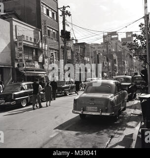 Degli anni Cinquanta, foto storiche di una strada nella città vecchia di Tokyo, Giappone, con molti più grande stile americano automobili dell'era parcheggiato a lato della strada. Foto Stock