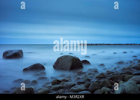 Pietre e sassi in una nebbia lattiginosa di onde. Una spiaggia guardando un porto naturale. Lunga esposizione. Foto Stock