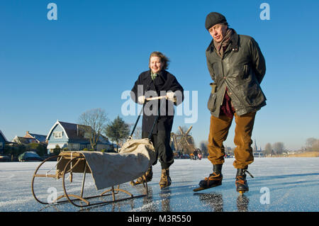 Coppia senior pattinaggio sul ghiaccio con i tradizionali pattini in legno e una slitta sul fiume de Vecht, Paesi Bassi Foto Stock