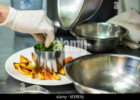 La mano dello chef aggiunge insalata di patate a fette sulla piastra Foto Stock