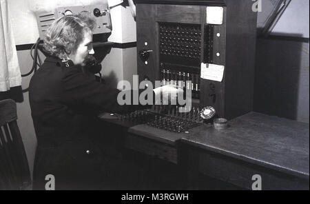 Degli anni Cinquanta, foto storiche che mostra una femmina in uniforme ufficiale di polizia azionando manualmente un centralino telefonico, Inghilterra, Regno Unito. In questo momento le chiamate dovevano instradato o collegato tramite una centrale di scambio telefono mediante l'uso del manuale degli operatori. Foto Stock