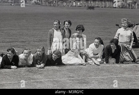 1955, foto storiche che mostra un gruppo di giovani bambini inglese, soprattutto bambine,seduto accanto a un'erba atletica o via di corsa per appoggiare i loro compagni di alunni di una scuola di sport giorno, Inghilterra, Regno Unito. Foto Stock
