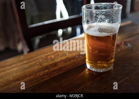 Mezza piena di pinta di birra sulla tabella pub Foto Stock