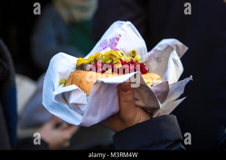 Mano che tiene un hot dog con condimenti (lingonberry e sottaceti) presso lo scandinavo Mercatino di Natale, London, Regno Unito Foto Stock