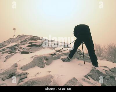 Fotografo di viaggio facendo le foto in antiche pietre sulla cima innevata della montagna. Inverno freddo e nebbiosa mattina in montagna Foto Stock