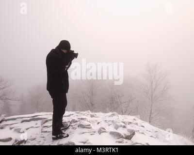 Fotografo di viaggio facendo le foto in antiche pietre sulla cima innevata della montagna. Inverno freddo e nebbiosa mattina in montagna Foto Stock