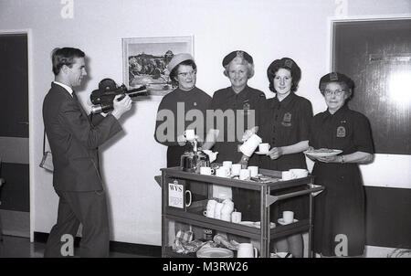 1955, storico, immagine mostra un cameraman filmare quattro volontari di sesso femminile delle donne del Volontariato (WVS) la carità in piedi accanto a un tè carrello. Fondata nel 1938 come le donne del volontariato per Air Raid precauzioni, la missione della WVS era - ed è ancora oggi - per aiutare, supporto e arricchire la vita delle persone anziane negli ospedali e nelle comunità. Foto Stock