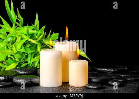 Spa composizione ramoscelli di bambù con la rugiada e candele su zen pietre di basalto, primo piano Foto Stock