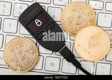 Trezor portafoglio hardware per cryptocurrency sulla tastiera con golden bitcoin monete e ethereum Foto Stock
