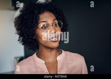 Sorridente imprenditrice africana con gli occhiali a parlare con un collega di lavoro in un ufficio moderno Foto Stock