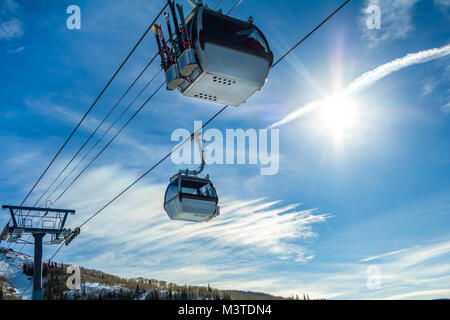 Due ski gondola cabine contro il cielo blu; sole luminoso sulla destra Foto Stock