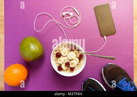 Farina di avena con frutti dopo un allenamento . Fitness e uno stile di vita sano concetto. Ciotola di fiocchi d'avena, arancio, mango, smartphone e sneakers Foto Stock