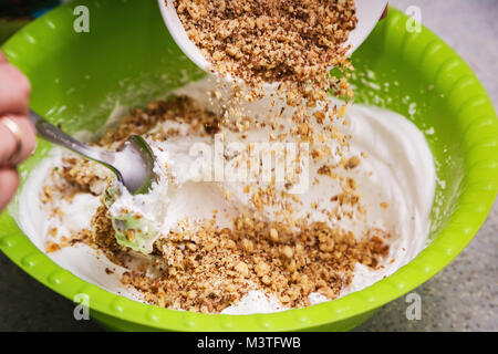 Noce lavorato viene versata in un recipiente con panna acida. È illustrato il processo di preparazione di una crema dolce per una torta a casa Foto Stock