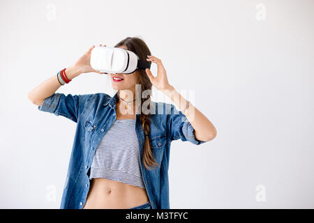 Ritratto di sorridente giovane donna prendere l'esperienza utilizzando occhiali VR su sfondo bianco. Femmina gioiosa toccando il dispositivo VR con le mani mentre experiencin Foto Stock