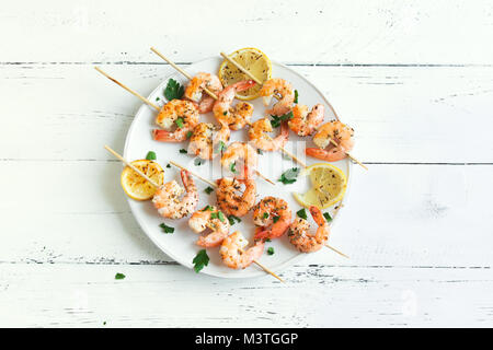 Grigliata di gamberi spiedini. Frutti di mare, shelfish. Gamberi spiedini con spezie e erbe aromatiche fresche in bianco sullo sfondo di legno, copia dello spazio. Gamberi b Foto Stock