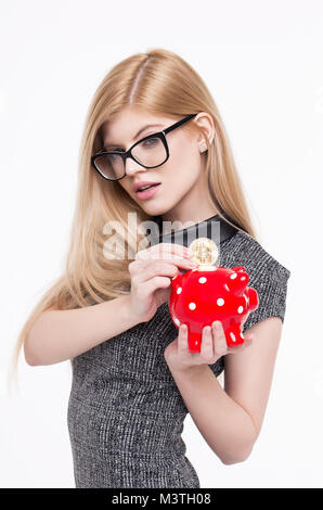 Smart giovane donna bionda mettere bitcoin nel salvadanaio, isolato su bianco Foto Stock