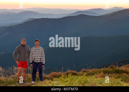 Due uomini viaggiatori sulla cima di una montagna un tramonto stupendo paesaggio. Gli amici gli escursionisti in piedi sulle montagne dei Carpazi colline con vista del tramonto o Foto Stock