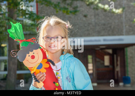 Ritratto di ragazza in piedi di fronte all'entrata della scuola e guardando avanti al suo primo giorno di scuola con un cono di caramelle in mano Foto Stock