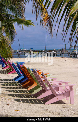 Verticalmente fila esposta delle colorate in legno sedie da spiaggia di fronte all'oceano. Foto Stock