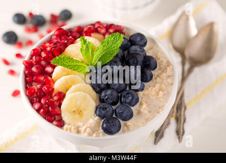 Ciotola di cereali con i semi di melograno, banana e mirtilli con la menta Sprg sulla parte superiore Foto Stock