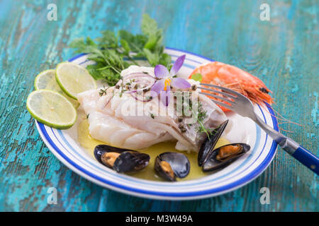 Merluzzo bianco Filetto di pesce, merluzzo bianco con frutti di mare mussells,gamberetti,calce e vegetali, sul blu sullo sfondo di legno Foto Stock