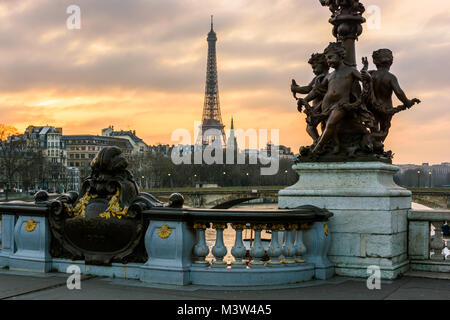 Vista della Torre Eiffel dal Pont Alexandre III al tramonto con il cherubs ornamenting uno dei suoi Art Nouveau lampione in primo piano. Foto Stock