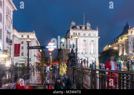 Persone con ombrelloni, Piccadilly Circus, pioggia, sera, ingresso della metropolitana di Londra, Regno Unito Foto Stock